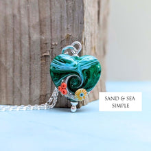 Load image into Gallery viewer, Heart-shaped pendant with beachy design on a chain, against a wooden and blue background with 'Sand &amp; Sea Simple' text.